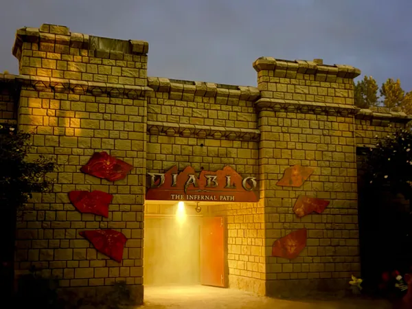 The Diablo: The Infernal Path maze entrance at Cedar Point: a floodlit castle wall with battlements and red rune panels, fog pouring out of the lit doorway