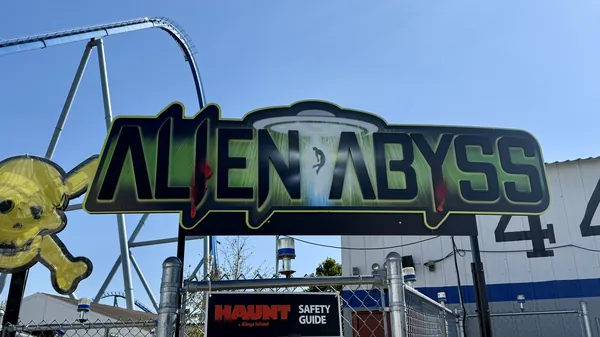 Green neon Alien Abyss maze sign with coaster track overhead at Kings Island