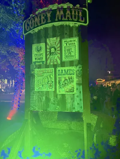 Coney Maul scare zone tower lit acid green at night at Kings Island, papered with circus sideshow posters