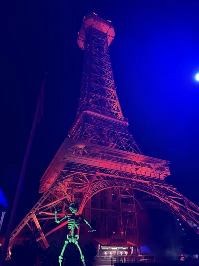 The Eiffel Tower at Kings Island floodlit red against a blue night sky, with a giant green skeleton at its base