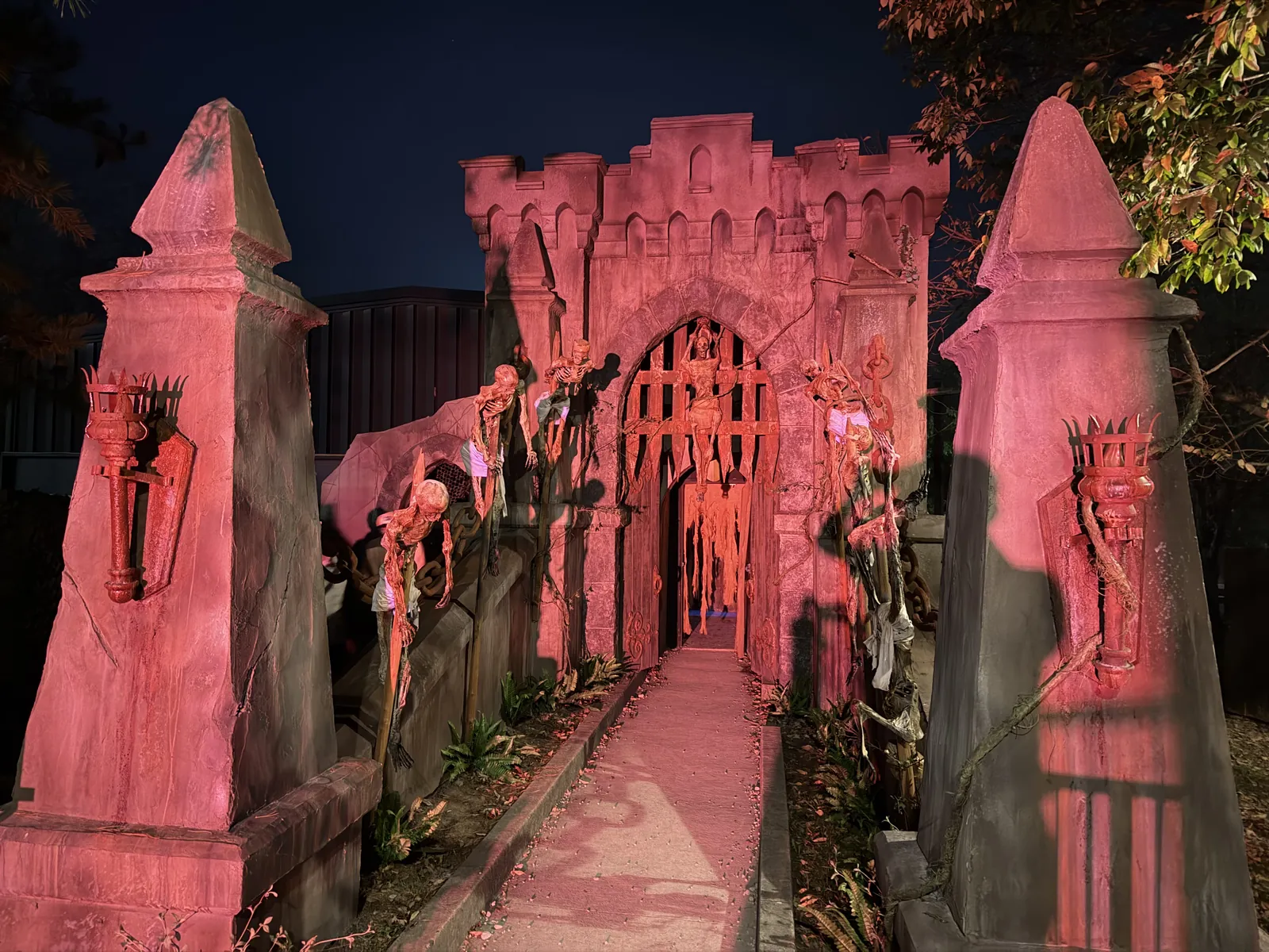 A red-lit stone castle gateway lined with impaled skeletons at Kings Island Halloween Haunt after dark