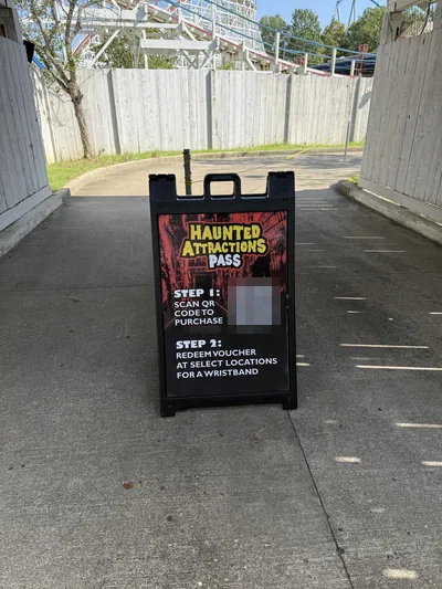 A-frame sign at Kings Island reading Haunted Attractions Pass, with a QR code to buy and instructions to redeem the voucher for a wristband