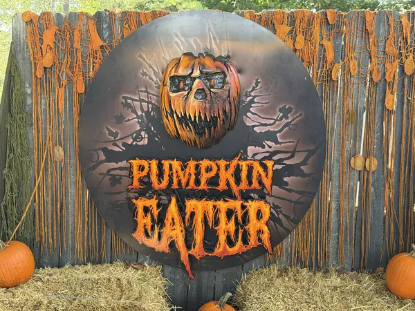 Round Pumpkin Eater scare zone sign on a wooden palisade fence with pumpkins and straw bales at Kings Island